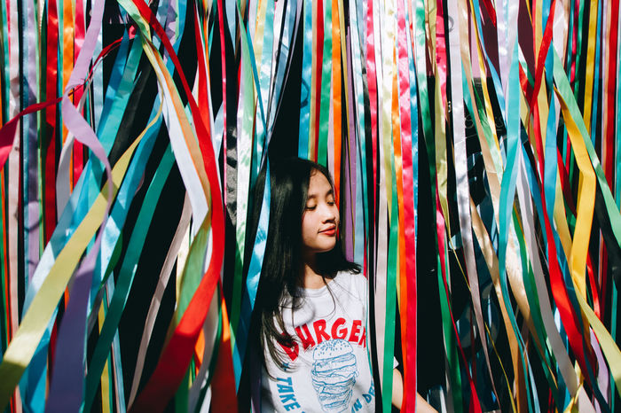 Young woman standing amidst colorful ribbons