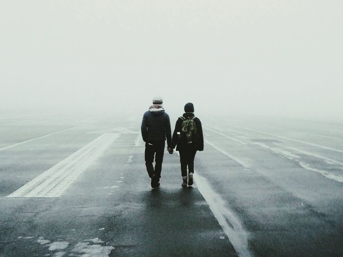 Rear view of man and woman walking on road against sky during winter