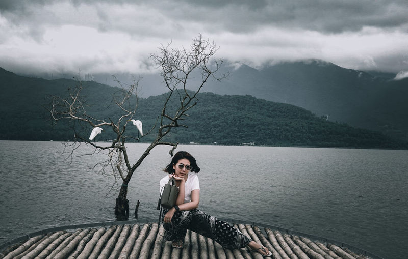 Full length of woman sitting by lake against mountains