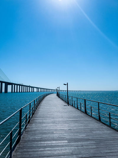 Blue on blue  sky and water with curving pier and bridges into the distance on bright sunny day