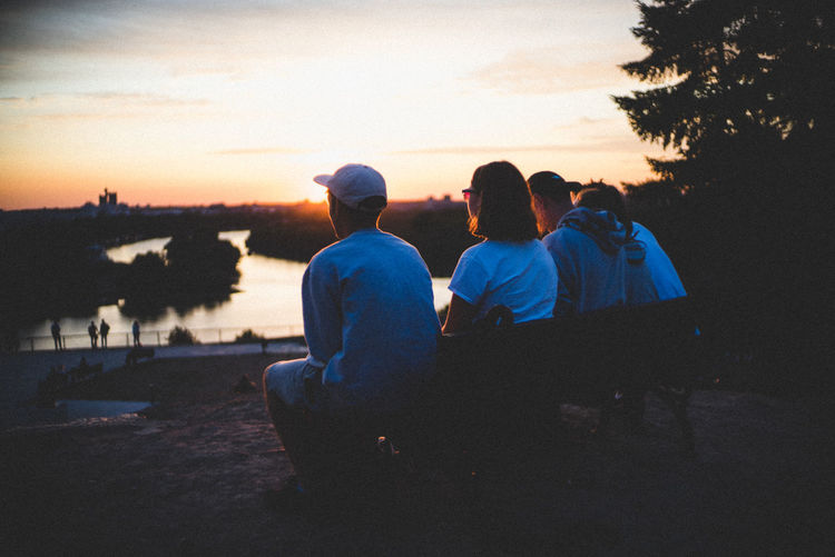 Rear view of couple sitting on rock against sky at sunset