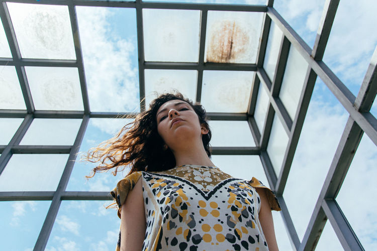 Low angle view of young woman standing by glass window