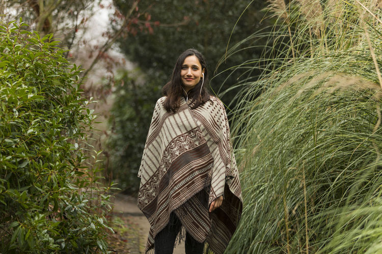 Portrait of smiling young woman wrapped in shawl standing amidst plants
