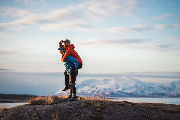 Woman giving man piggyback with mountains behind them
