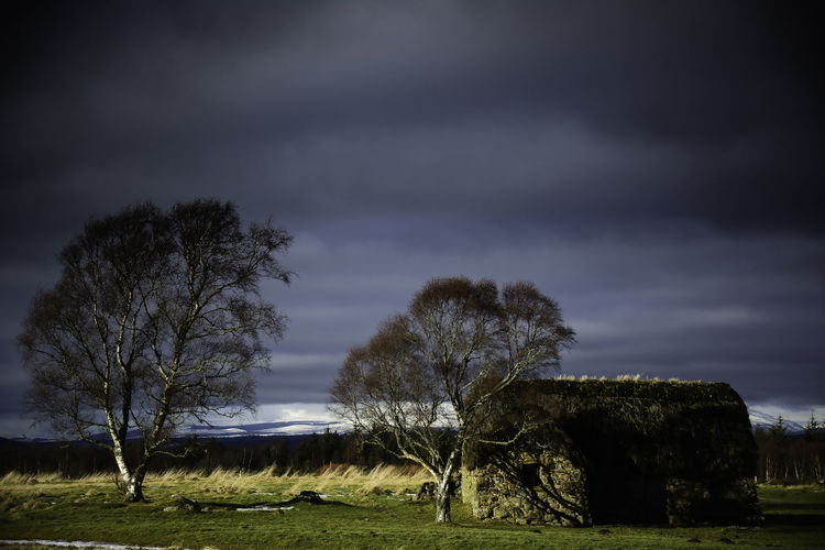 Leanach cottage on field against cloudy sky at scottish highlands