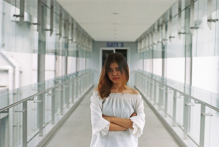 Portrait of young woman with arms crossed standing in corridor