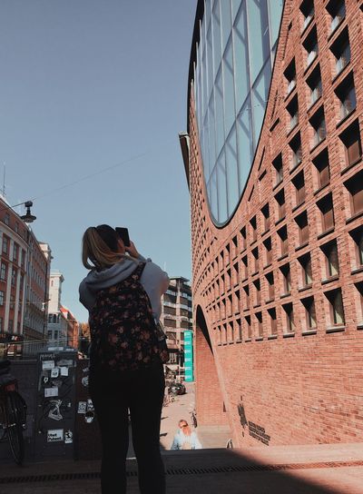 Rear view of woman standing by buildings against clear sky
