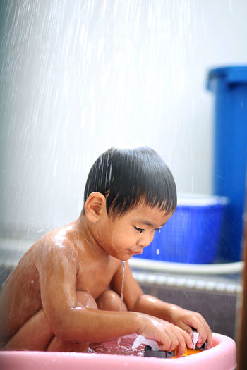 Shirtless boy playing while bathing in bathtub