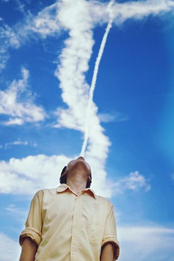 Optical illusion of vapor trail from man standing against sky