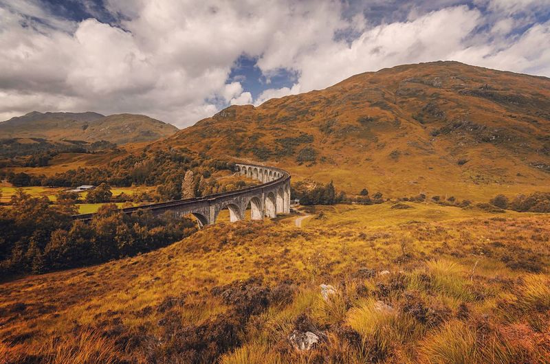 Bridge over field against cloudy sky at glenfinnan