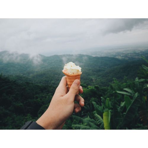 Cropped hand of person holding ice cream against landscape