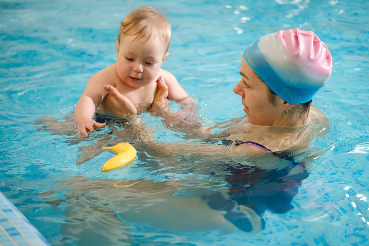 Early age swimming in pool. baby boy trained to swim in water. happy child with trainer woman in