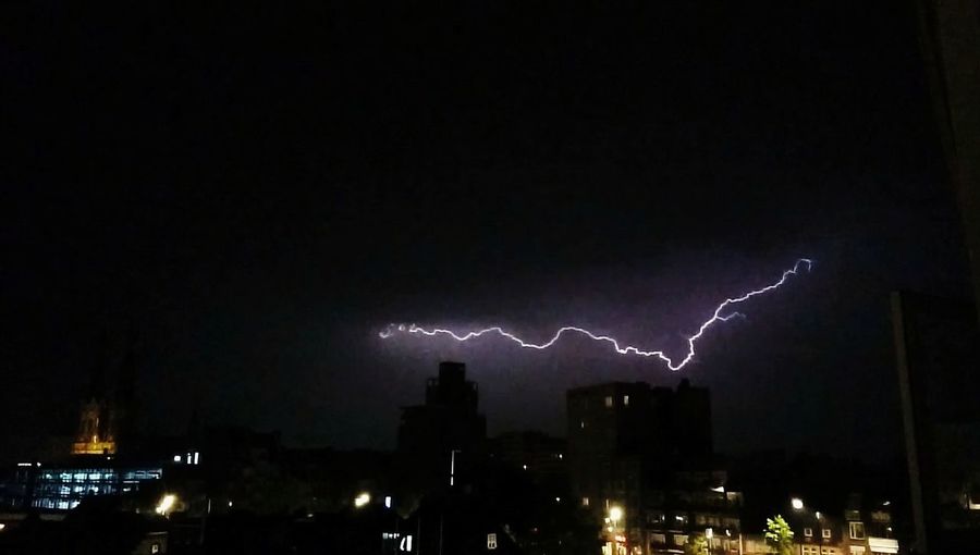 Lightning over illuminated cityscape against sky at night