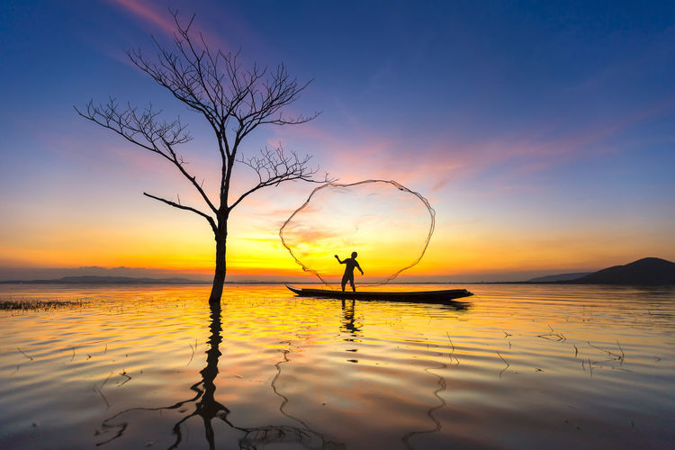 Silhouette fisherman fishing on sea during sunset
