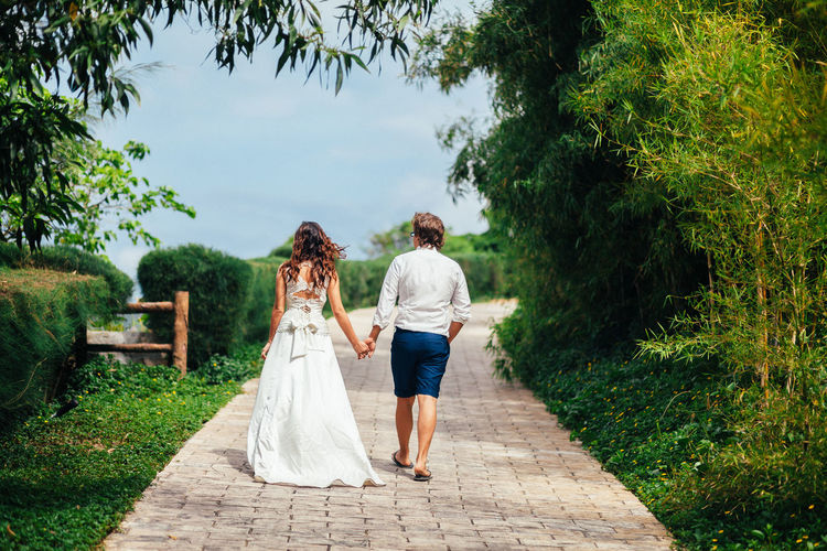 Rear view of bride and groom walking on footpath