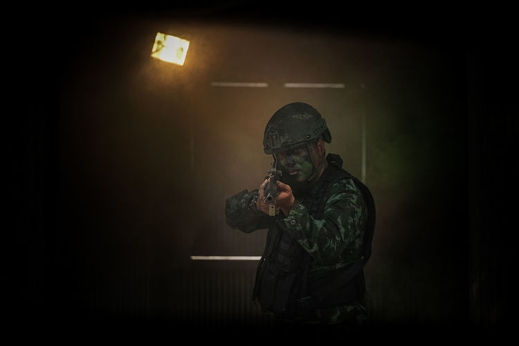 Portrait of soldier holding gun standing in darkroom