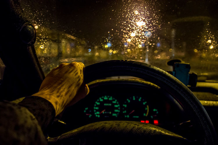Close-up of human hand driving car at night during rainfall