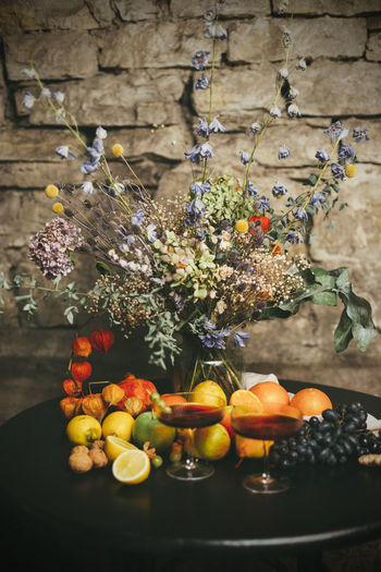 Dry flowers in vase on table with fruits and red wine