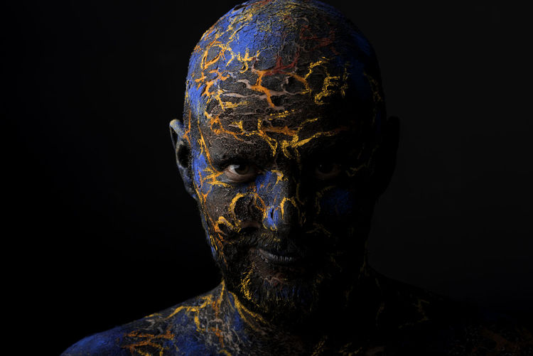 Close-up portrait of mid adult man with body paint standing against black background
