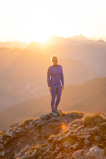Woman standing on mountain peak against sky during sunrise