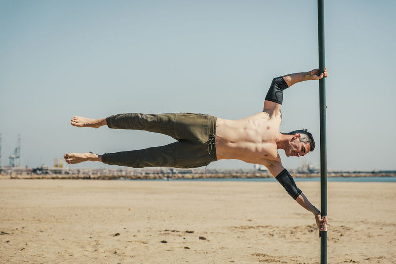 Male sportsperson doing exercise while balancing on bar at beach