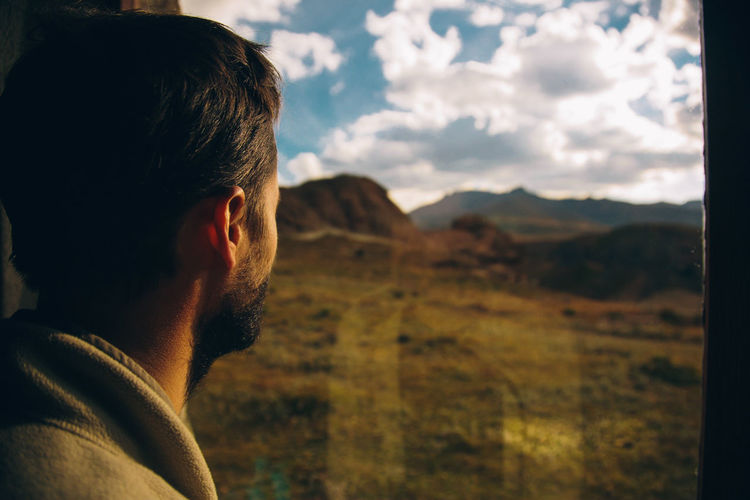 Rear view of man looking at mountains against cloudy sky