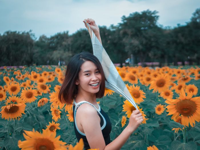 Young woman holding handkerchief while standing amidst sunflowers on field