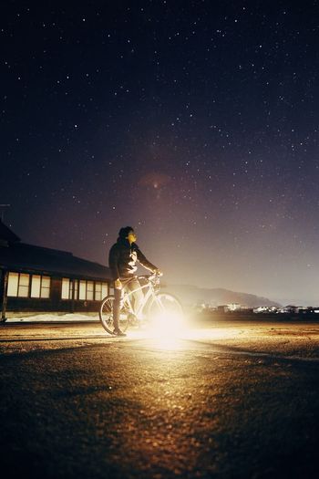 Person riding bicycle on illuminated road against star field