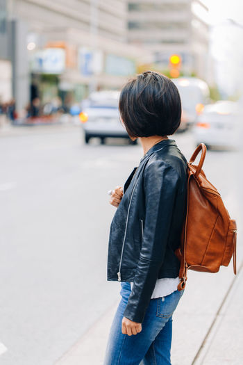 Side view of young woman standing on road in city