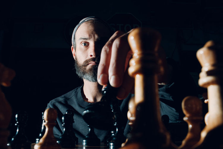Portrait of man playing chess against black background