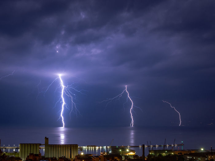 Lightning over sea by illuminated city at night