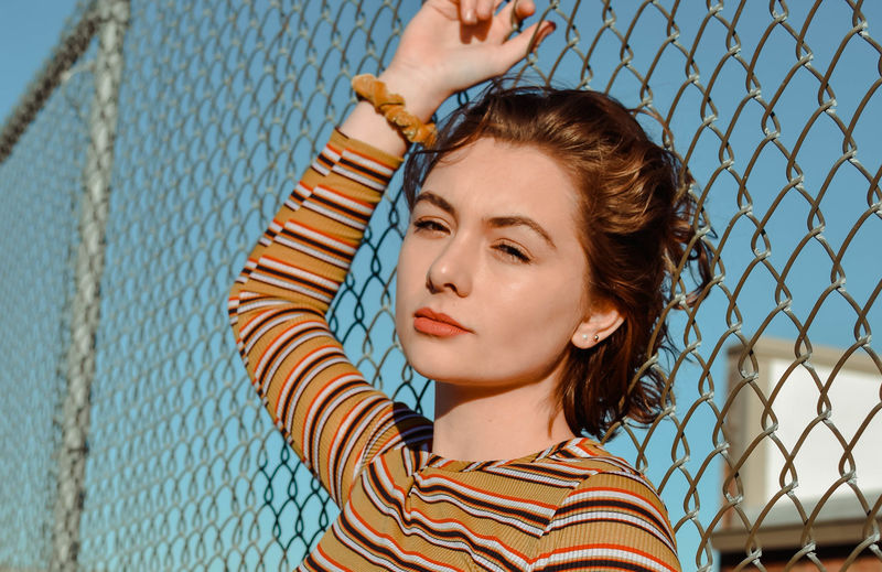Portrait of young woman looking through chainlink fence
