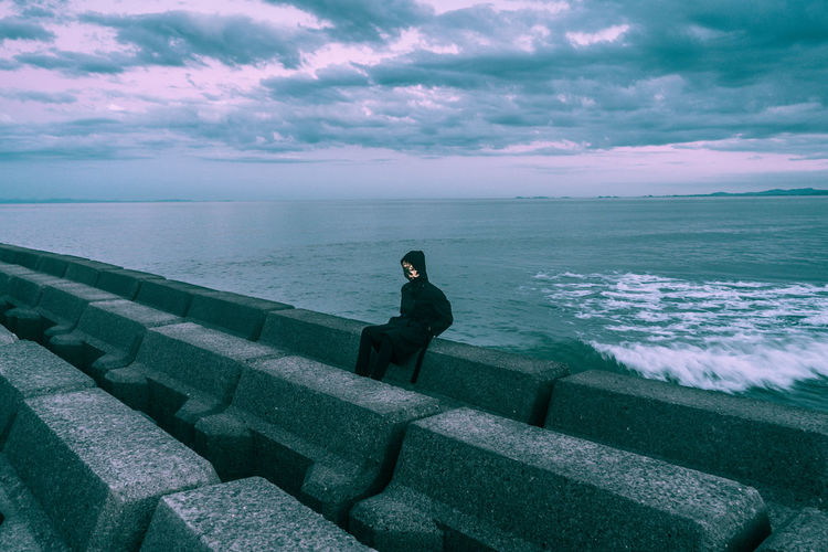 Man wearing mask while sitting against sea and sky