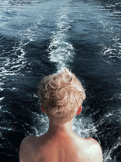 Rear view of shirtless boy against sea