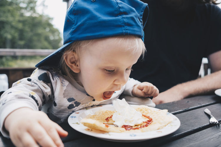 Girl with mouth open looking at food while sitting by father at table