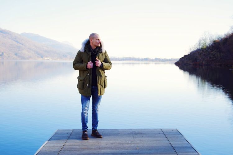 Full length of man standing on pier by lake against clear sky during winter