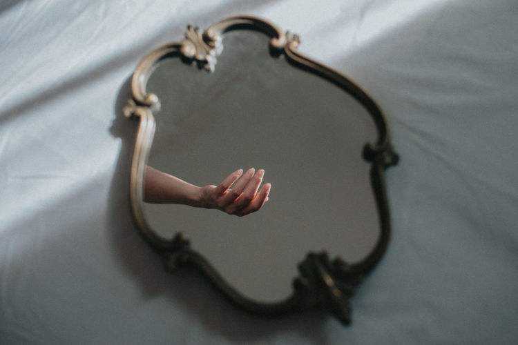 Reflection of woman hand in mirror on bed