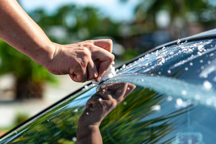 Cropped image of hand holding leaf against car