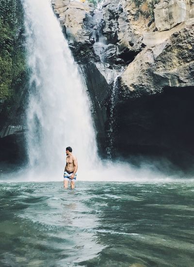 Shirtless man against waterfall in forest