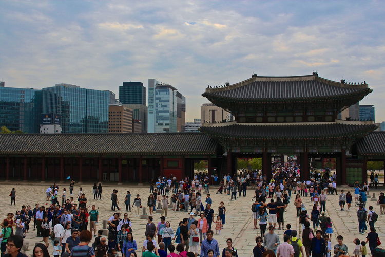 Crowd visiting gyeongbokgung by modern buildings against sky