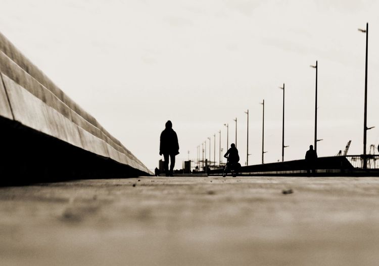 Silhouette people walking on bridge against sky