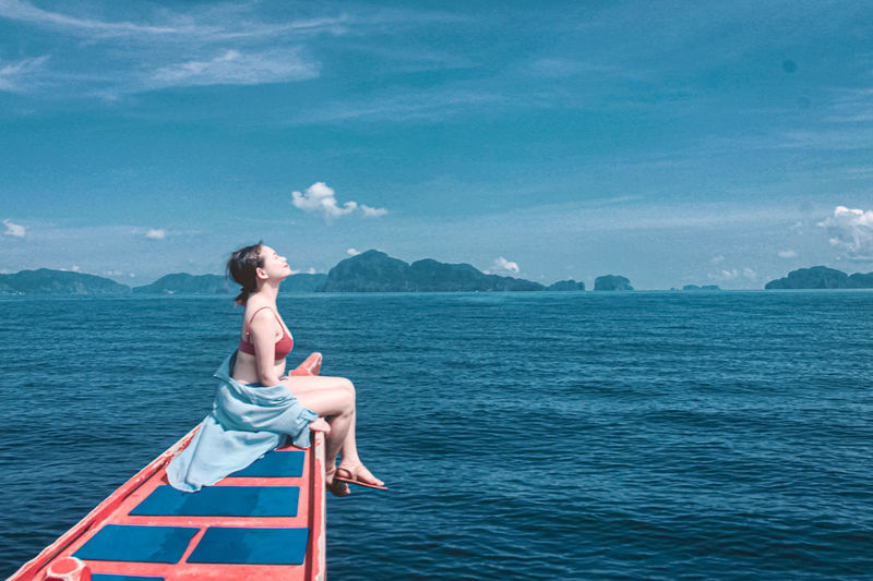 Young woman sitting in sea against sky
