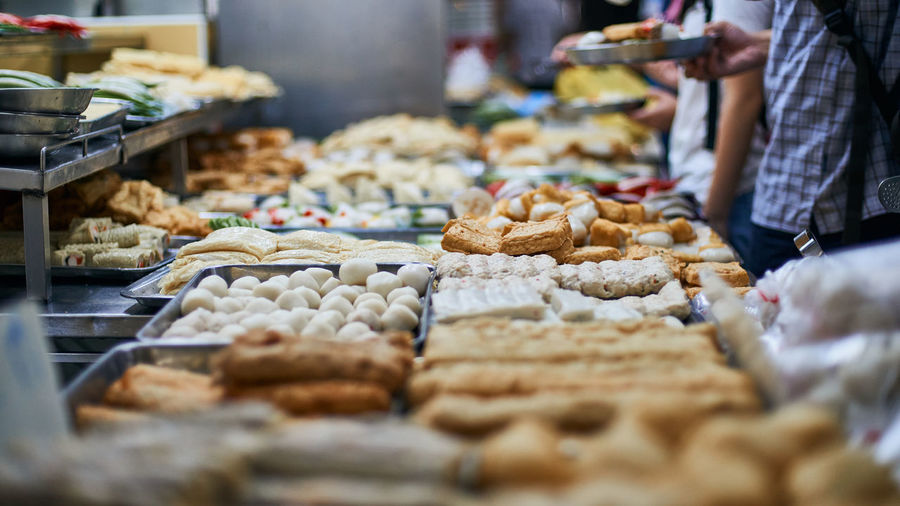 Customers standing around food and fishballs for sale at market stall