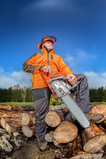 Low angle view of man standing on logs against sky