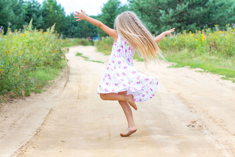 A girl with long blond curly hair is dancing, spinning on a forest road. freedom of movement. 