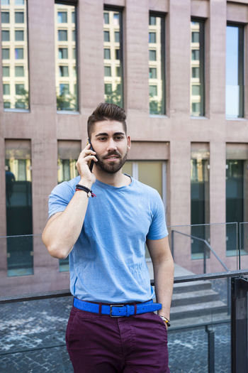 Young businessman talking on phone while standing against building in city
