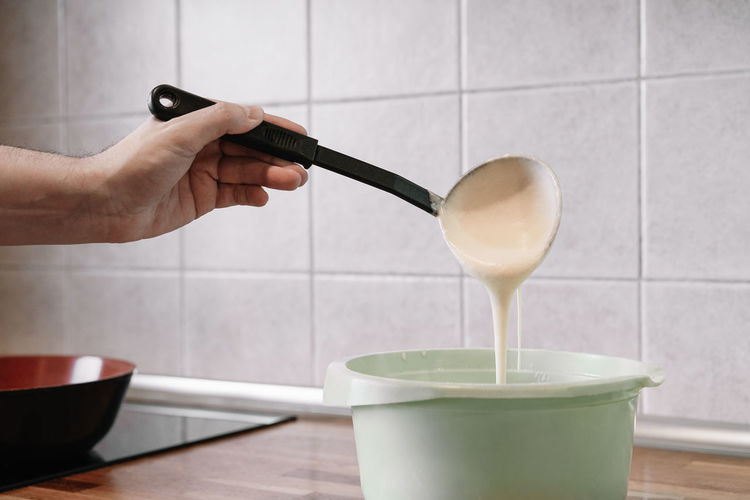 Cropped image of person pouring dough in bowl