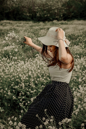 Side view of woman wearing hat standing amidst flowers