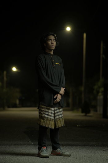 Young man looking away while standing on street at night