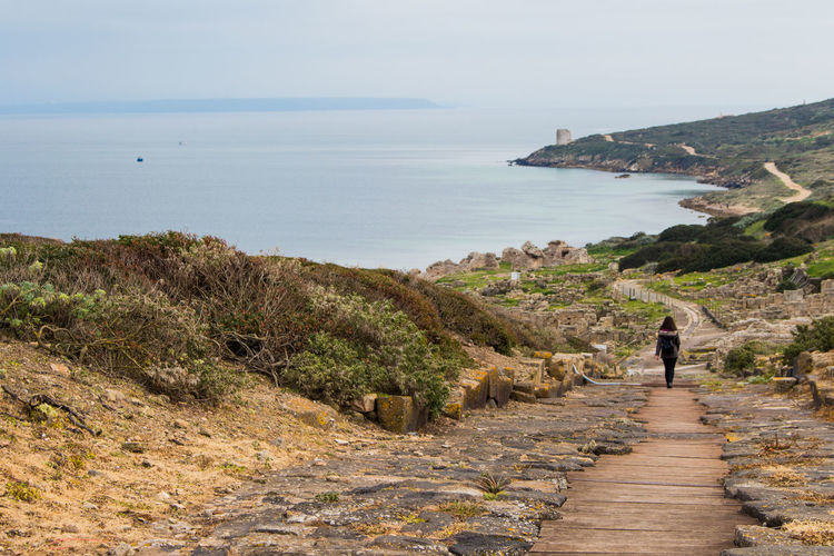 Woman walking on footpath against sea